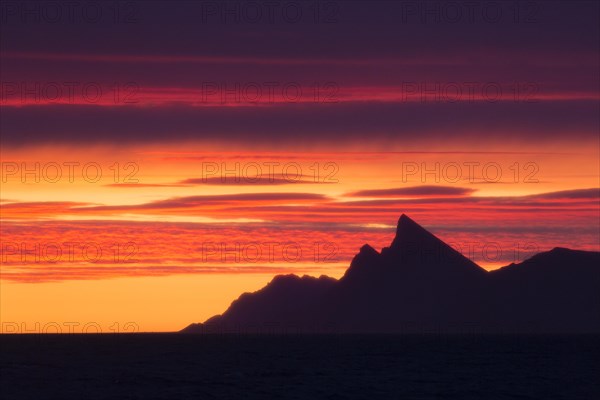 Mountain at Kongsfjorden silhouetted against colourful sunset in summer