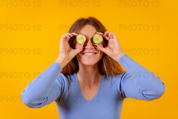 Vegan woman with cucumber slices on her eyes on a yellow background