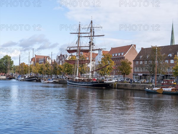 Historic sailing ships on the banks of the river Trave and behind them the brick buildings Old Hanseatic Houses in the Unesco World Heritage Site Luebeck