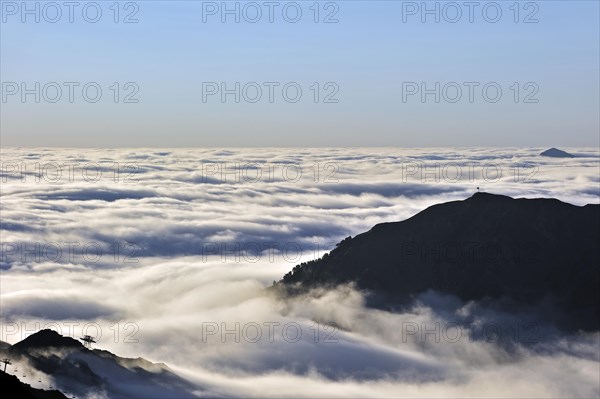 View over silhouetted chairlifts and mountains covered in mist at sunrise seen from the Col du Tourmalet