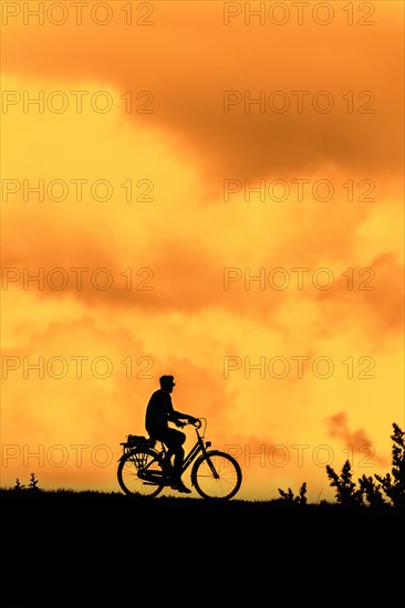 Male cyclist riding his bicycle silhouetted against orange sunset sky in summer