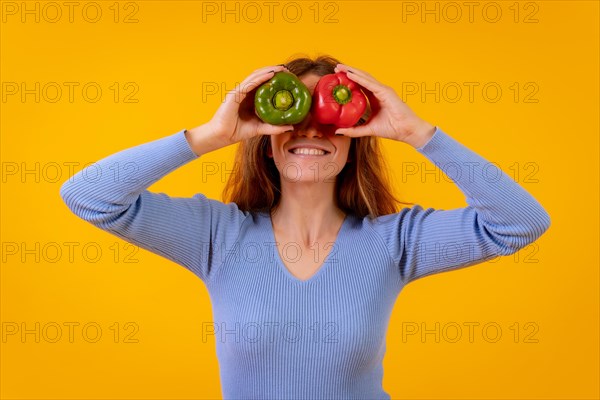 Vegetarian woman in a portrait with peppers in her eyes on a yellow background