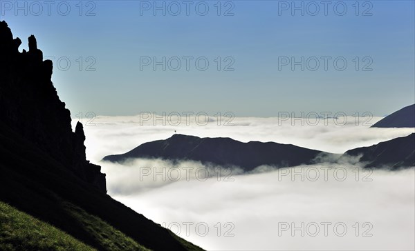 View over silhouetted jagged mountain edge and mountains covered in mist at sunrise seen from the Col du Tourmalet