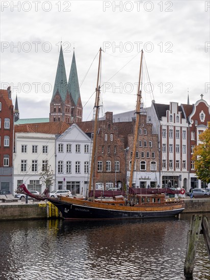 Historic sailing ships on the banks of the river Trave and behind them the brick buildings Old Hanseatic Houses in the Unesco World Heritage Site Luebeck