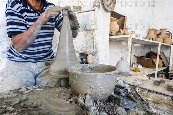 Skillful potter forming a vessel out of gray clay in a pottery factory