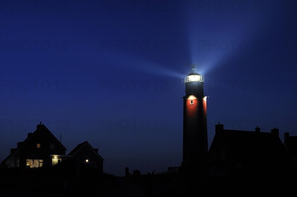 Houses and light beams from lantern of the Cocksdorp lighthouse Eierland at night