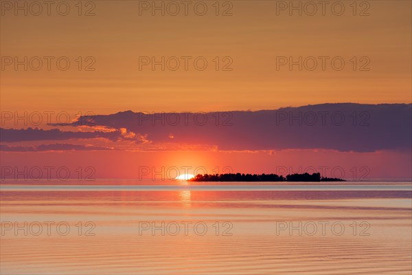 Sunset with sun setting behind silhouetted island in Lake Vaenern