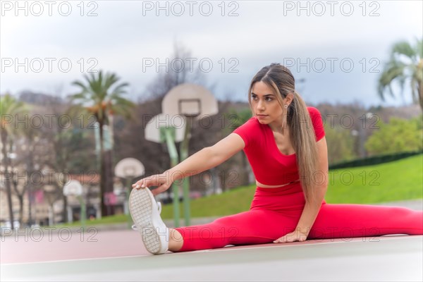 Fit woman in red outfit stretching on a basketball court