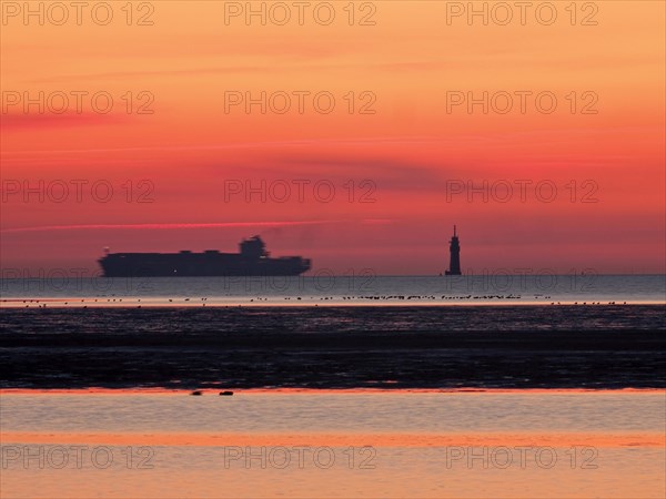 Container freighter on the Outer Weser with lighthouse in the evening light