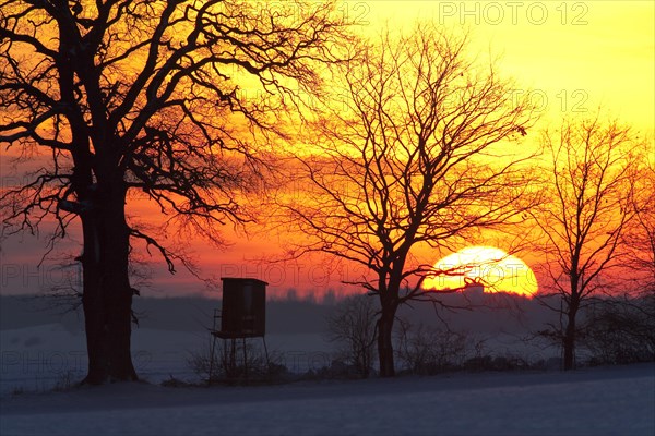 Raised stand for hunting deer in field in the snow in winter silhouetted against sunset