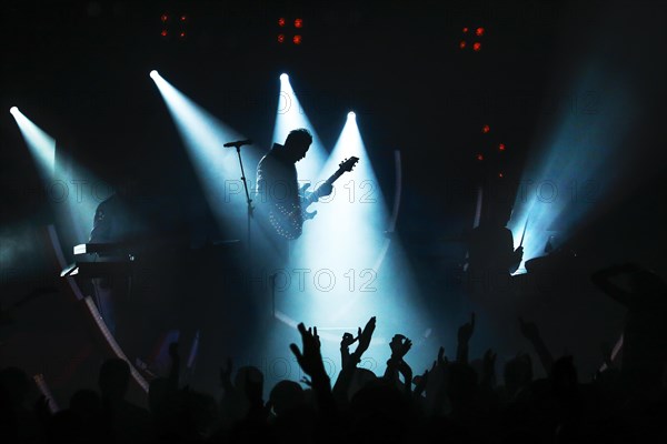 Electric guitar player of rock band in blue spotlight during pop concert