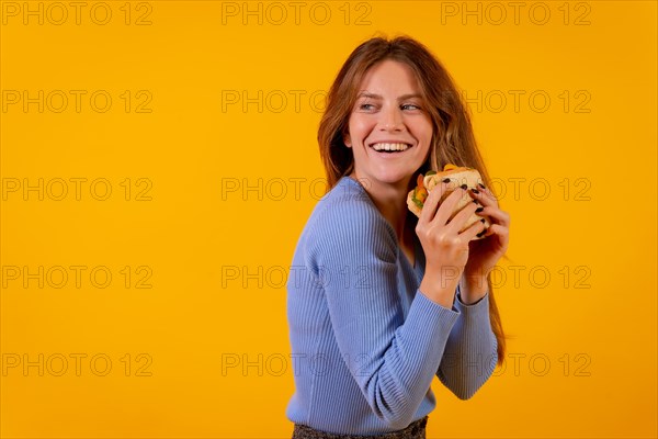 Cheerful woman eating a sandwich on a yellow background