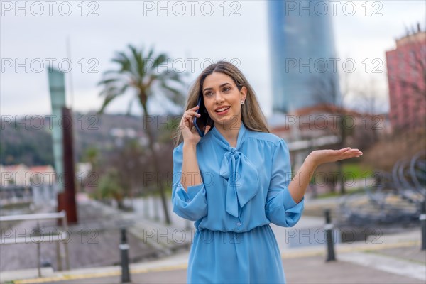 Blonde woman in blue dress smiling talking on the phone walking in the city
