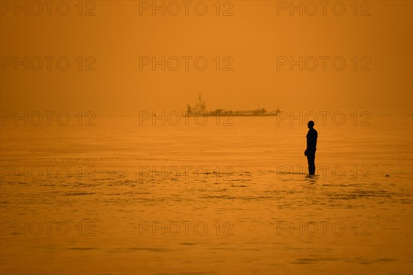 Sculpture Another Time XVI by Antony Gormley silhouetted against sunset along the North Sea coast at Knokke-Heist