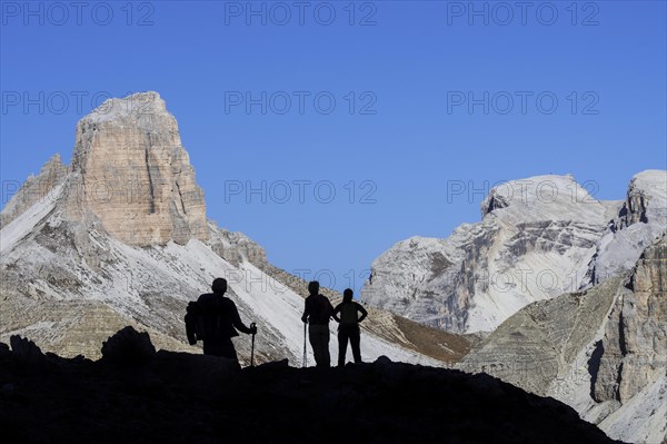 Three mountain walkers silhouetted against Torre dei Scarperi