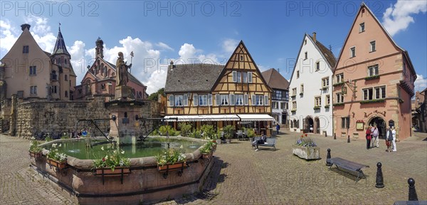 Panoramic photo of the Fontaine de Saint-Leon on the Pl. du Chateau Saint-Leon square with neo-Romanesque-Byzantine St. Leo Chapel and with medieval colourful buildings around the square in the centre of the old town