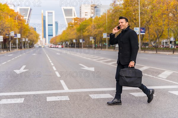 Middle-aged Caucasian businessman talking on the phone at a city zebra crossing