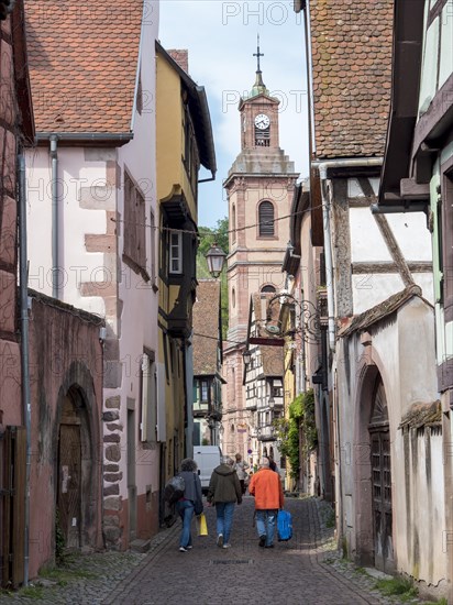 The narrow Rue de la 1E Armee street with tourists and in the distance the bell tower and the Eglise protestante Sainte-Marguerite Protestant Church