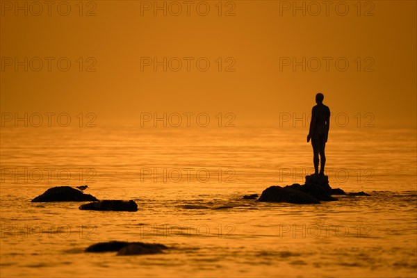 Sculpture Another Time XVI by Antony Gormley silhouetted against sunset along the North Sea coast at Knokke-Heist
