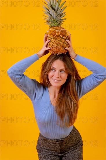 Woman with a pineapple in sunglasses in a studio on a yellow background