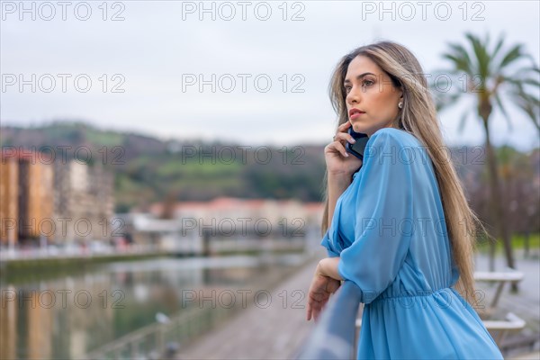 Blonde woman in blue dress with phone on the city river
