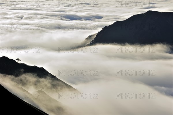 View over silhouetted chairlifts and mountains covered in mist at sunrise seen from the Col du Tourmalet