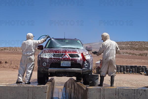 Bolivian men in protective suits washing a car