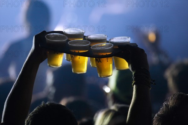 Ambiance during live rock concert and man bringing beer in plastic cups to friends among spectators
