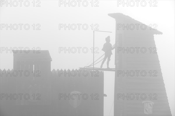Medieval siege weapons and wooden attack tower silhouetted in the mist at the mediaeval fortified village Larressingle in the Pyrenees