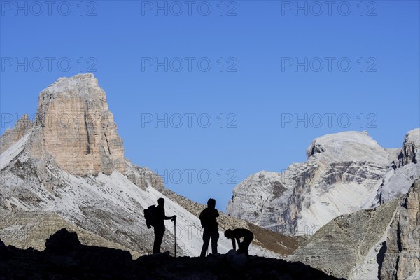 Three mountain climbers silhouetted against Torre dei Scarperi