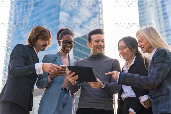 A group of multi ethnic business people in a business park smiling looking at a tablet