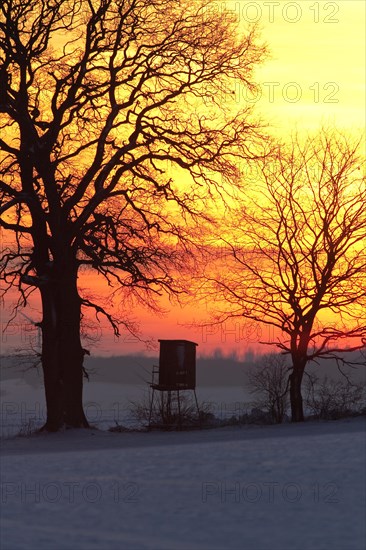 Raised stand for hunting deer in field in the snow in winter silhouetted against sunset