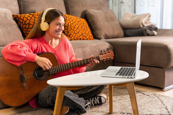 Woman learning to play the guitar at home with online classes on the computer