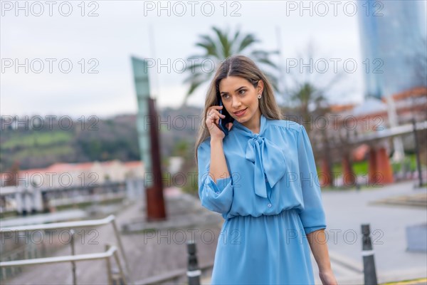 Blonde woman in blue dress talking on the phone walking in the city