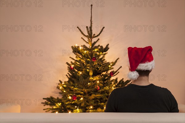 A man sits on a sofa in front of a Christmas tree