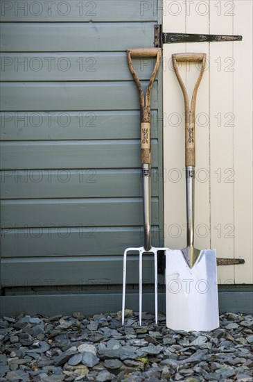 Garden fork and spade leaning against a painted shed