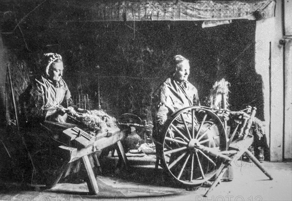 Early 20th century photograph showing two old female home spinners using wooden spinning wheel and hackle