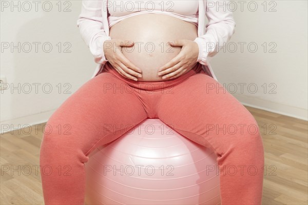 Pregnant woman sitting on exercise ball with hands on baby belly | MR:yes NH_pregnant_belly_mr