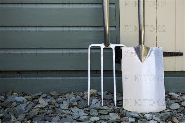 Garden fork and spade leaning against a painted shed