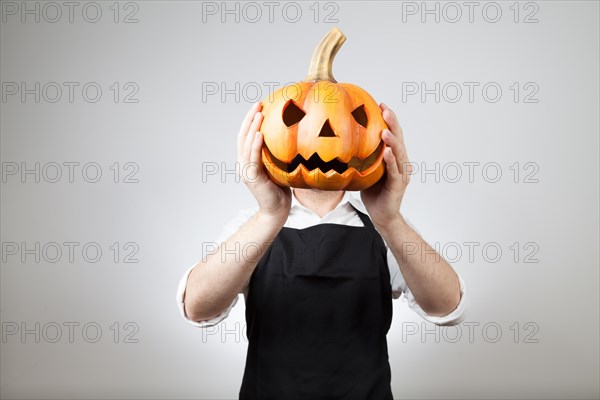 Man with apron holds a clay pumpkin in front of his head | MR:yes ph_halloween_mr