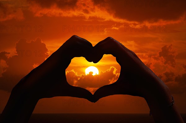 Hands form a heart in front of a sunset