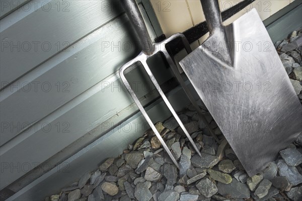 Garden fork and spade leaning against a painted shed