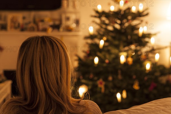 Woman sitting on sofa in front of Christmas tree