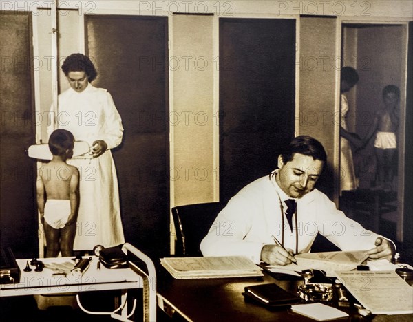 Old sepia archival photograph showing doctor and nurse examining school children in their underwear at dispensary in the 1950s