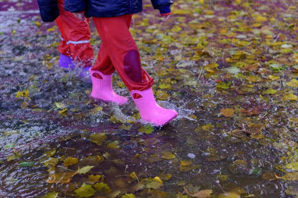 Two children walking through a puddle of water with their boots on a rainy day