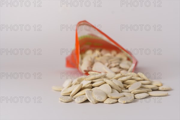 Roasted pumpkin seeds with salt coming out of their red bag on a white table with copy space