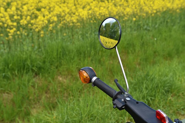 Rear view mirror of moped Schwalbe from the GDR in front of a rape field