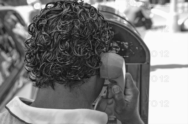 Black-haired New Yorker making a phone call at a telephone pillar