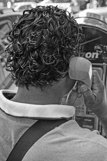 Black-haired New Yorker making a phone call at a telephone pillar