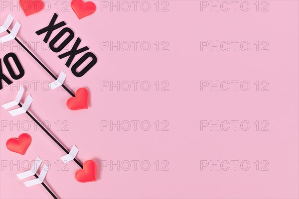 Valentine's day flat lay with cupid's love arrows and text XOXO on pink background with copy space